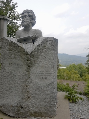 Statue of Hephaestus, god of blacksmiths, sculptors, volcanoes, and fire in front of gray, smoky skies